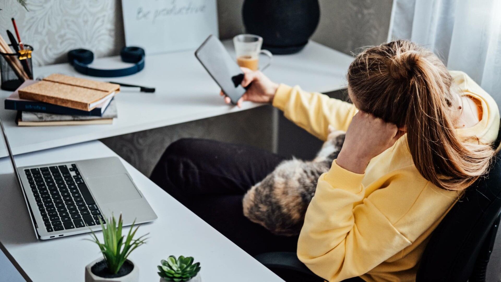 A female employee sitting at her desk in the office experiencing a distraction via her cellular device.