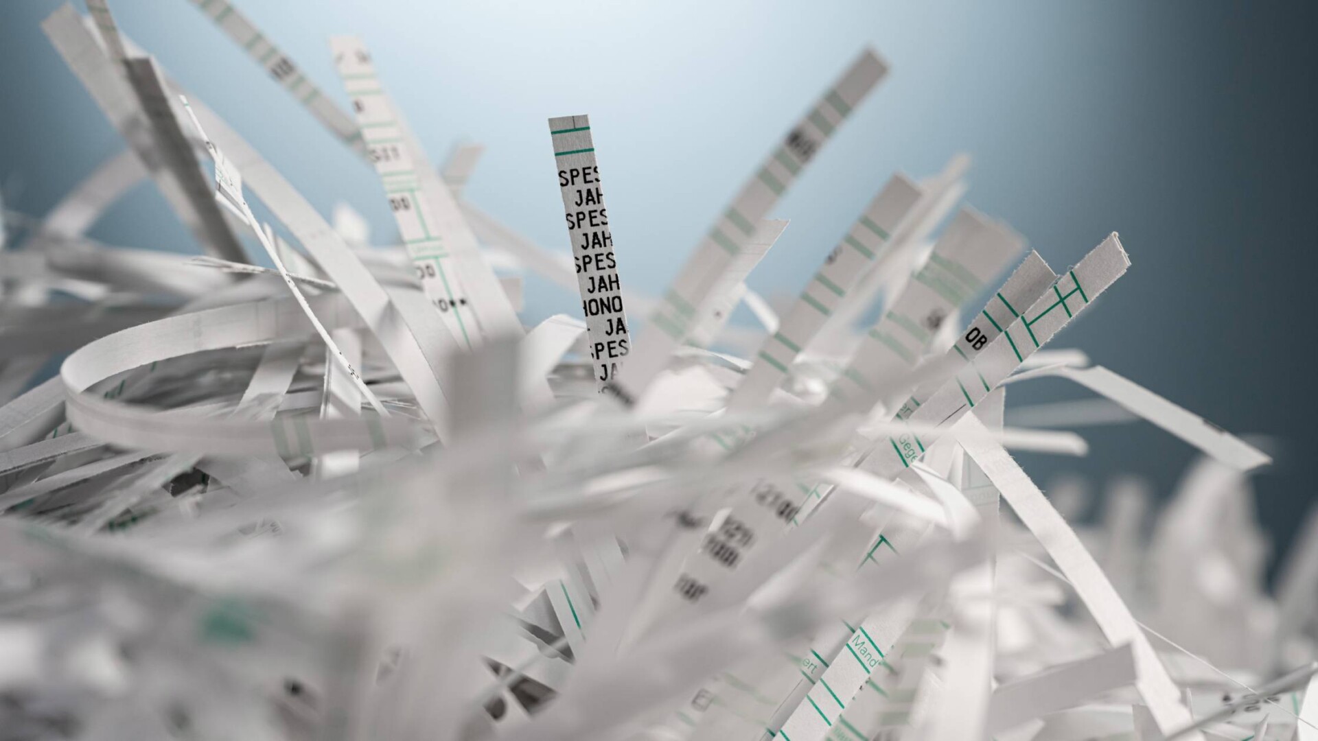 A pile of shredded documents containing sensitive information. The shredded documents are in front of a blue backdrop.