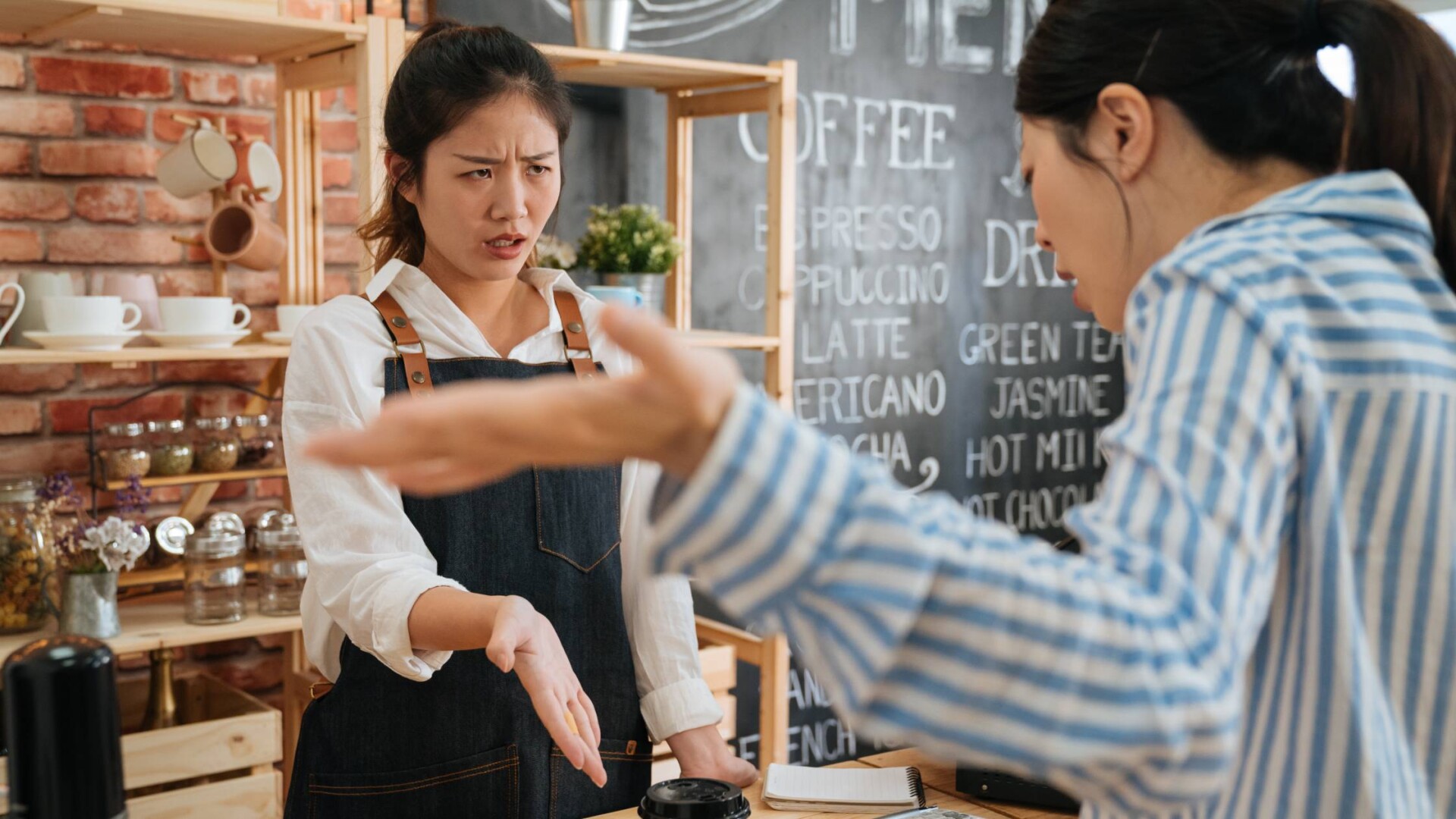 A small business owner arguing with a dissatisfied customer about their service and product. The worker is wearing an apron.