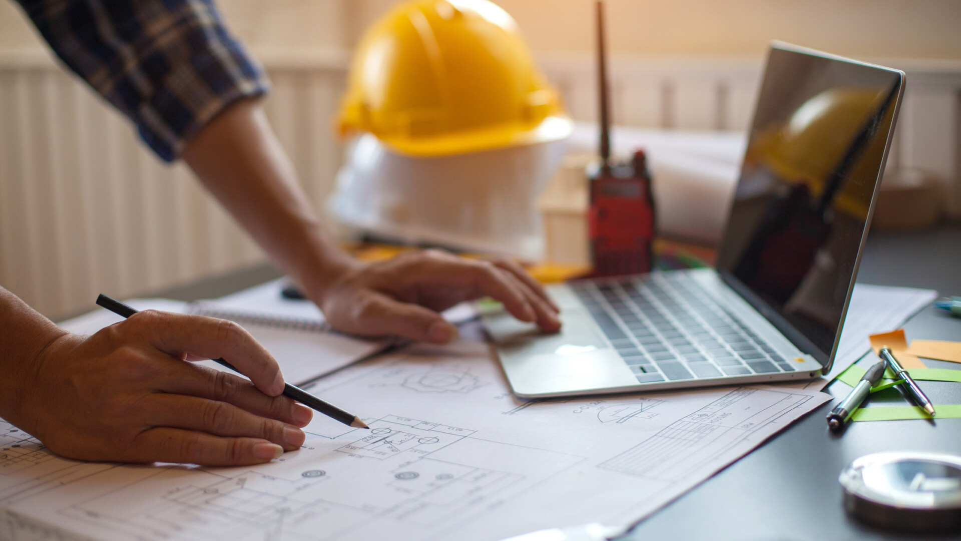 An architect is designing a commercial building. He is sketching out the design next to his laptop on the table.
