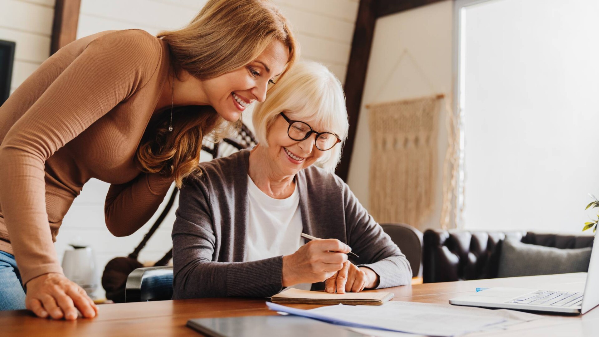 An aging mother and her adult daughter at the table together talking about family estate plans. The mother has a document.