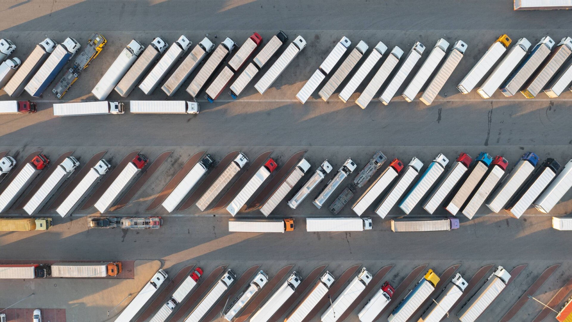 A bird’s eye view of a large parking lot. A fleet of commercial trucks with loaded cargo occupy the lot.