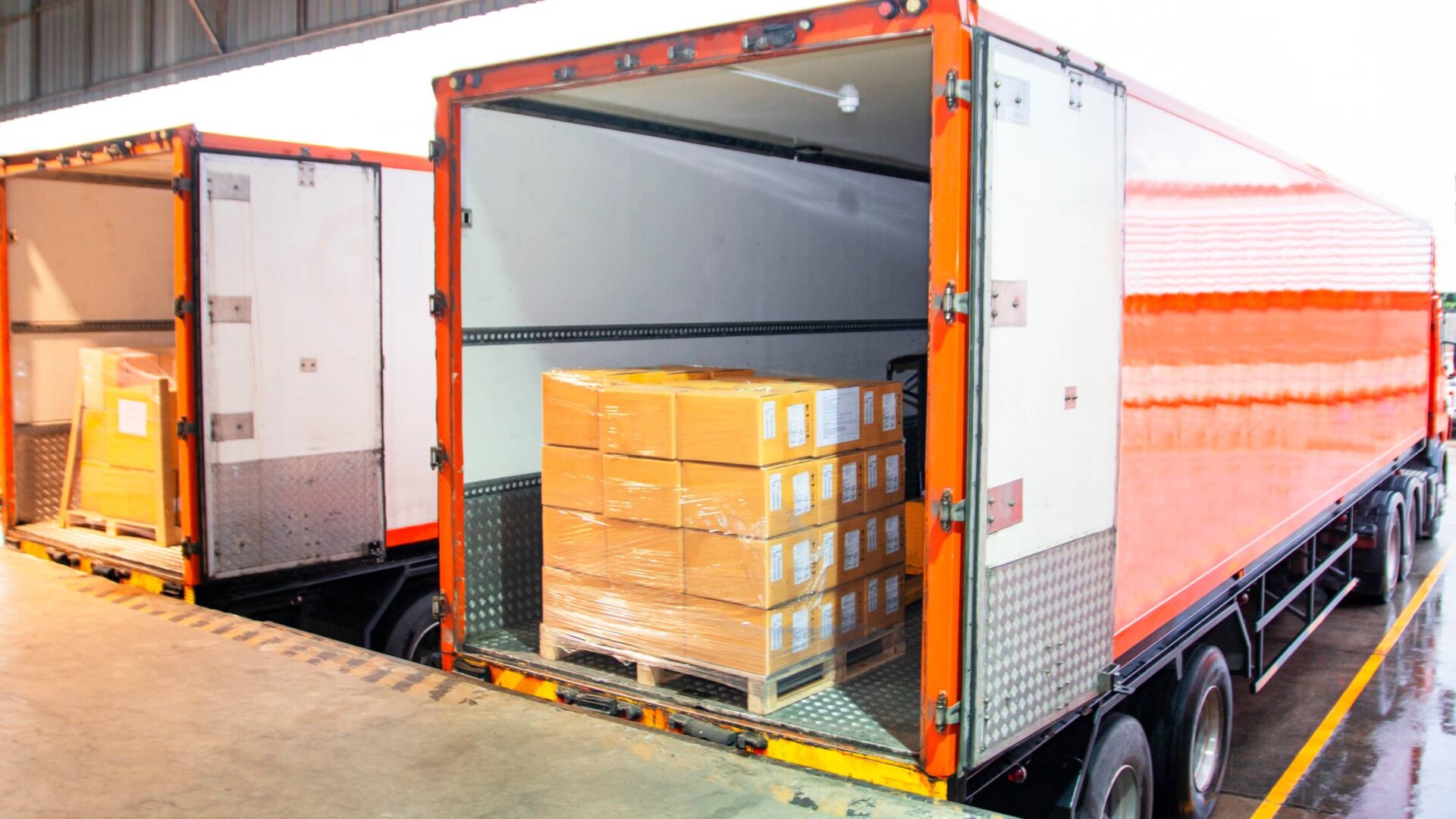 Two shipping trucks with their cargo bed open. Inside, there is freight wrapped in plastic wrap sitting on a wooden pallet.