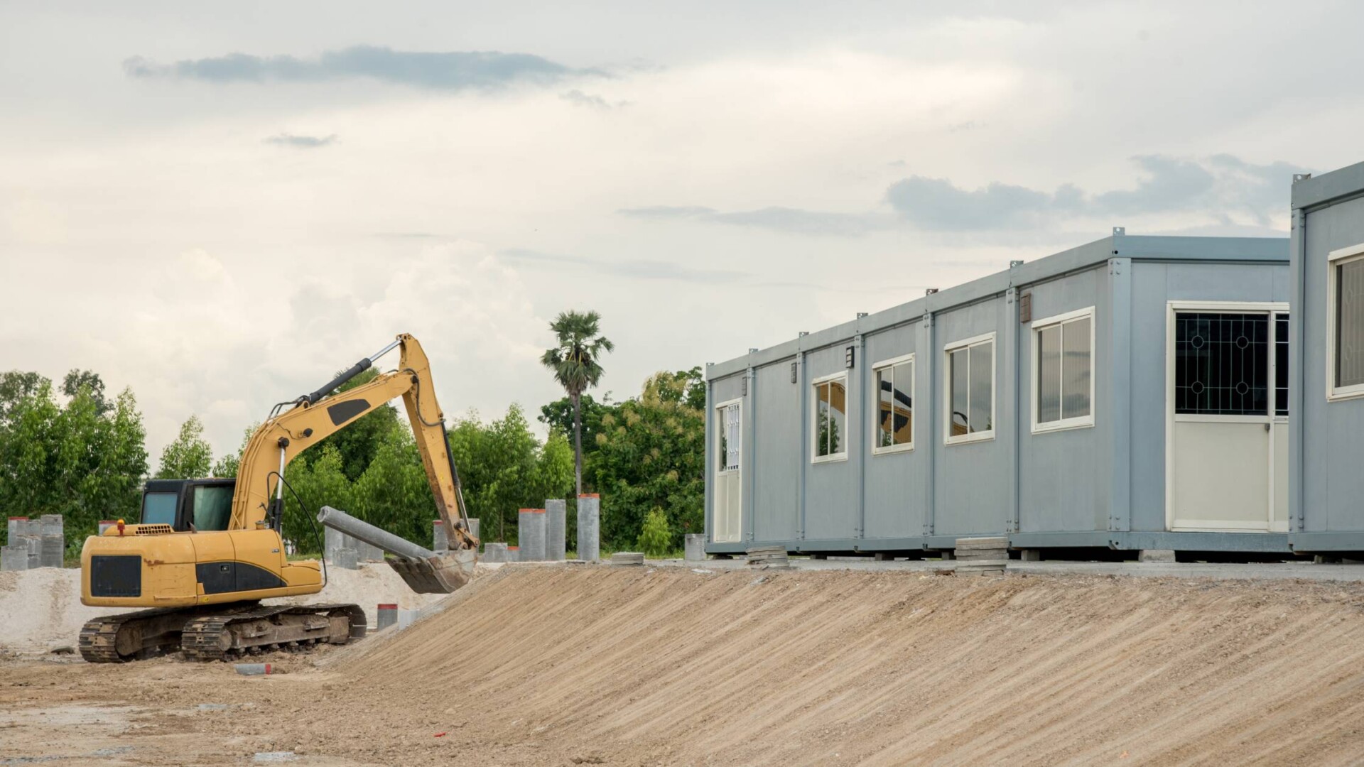 Mobile buildings on a construction site with an excavator nearby. The buildings are placed at a higher elevation.