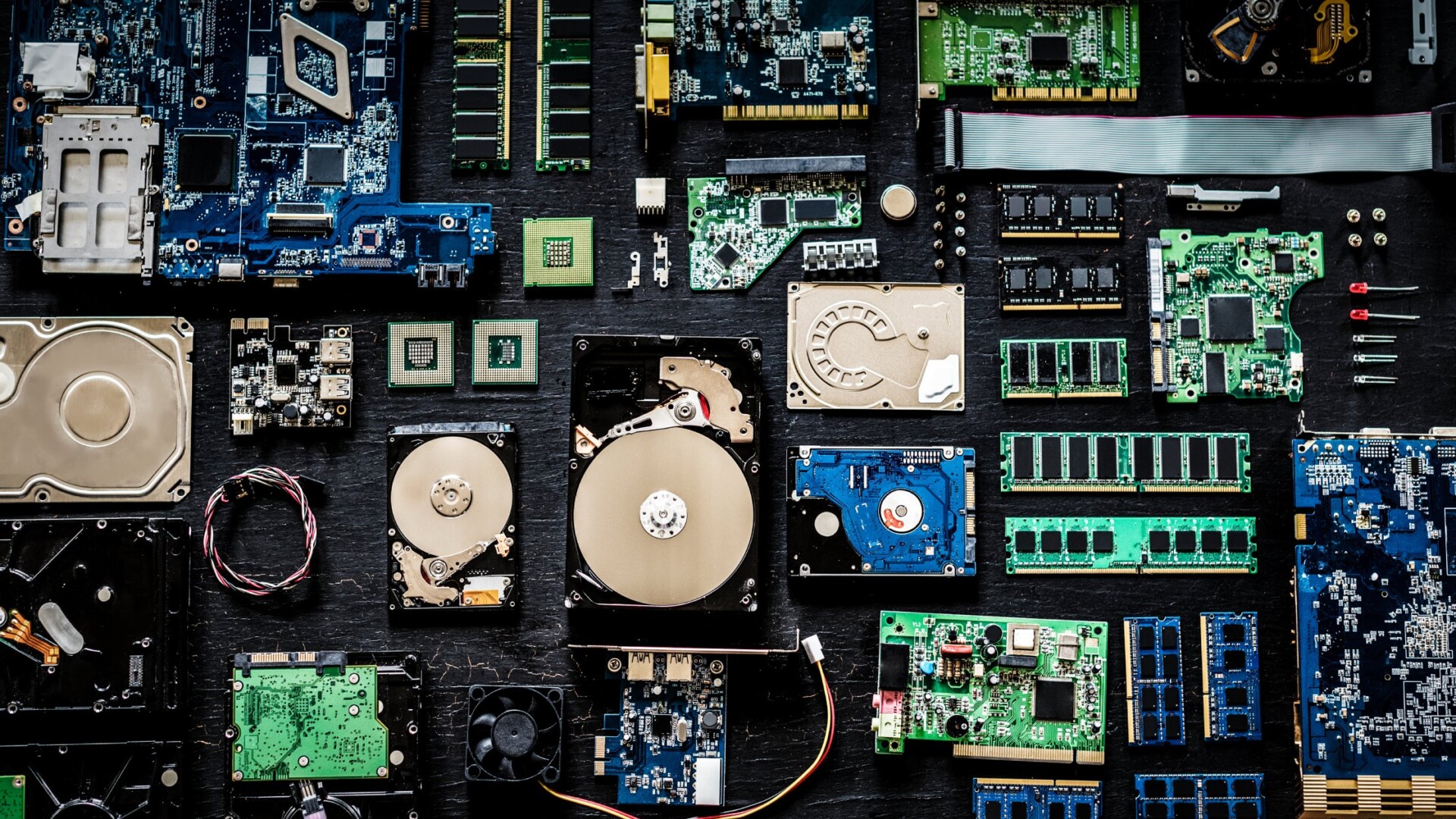 Various computer parts, including hard drives and motherboards, neatly laid out on a black wood surface.
