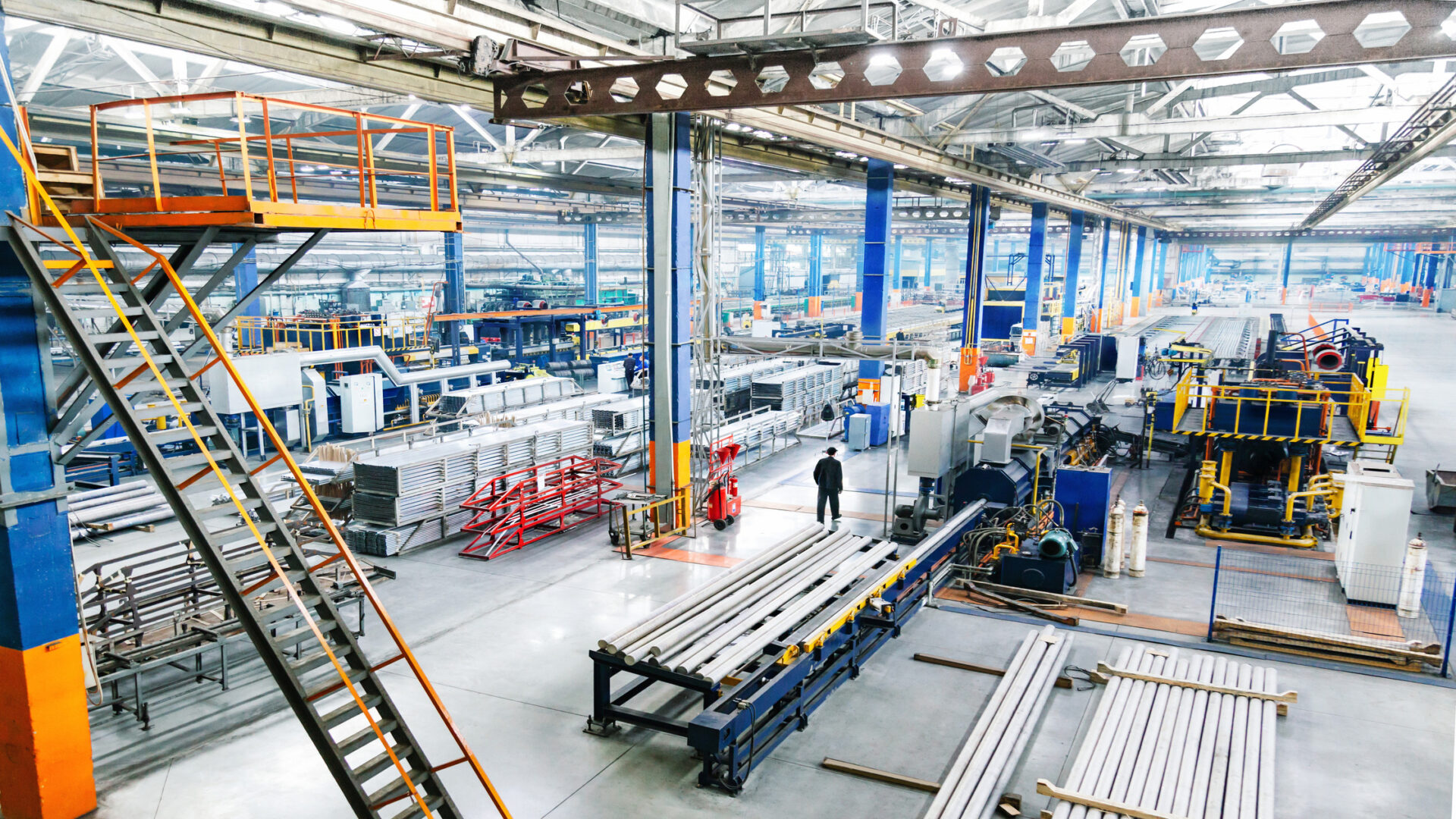 A large industrial warehouse with stairways and machinery on the work floor. There's an employee walking in the center aisle.