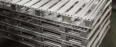 A close-up of five large aluminum metal pallets stacked together on a black concrete floor in a building.
