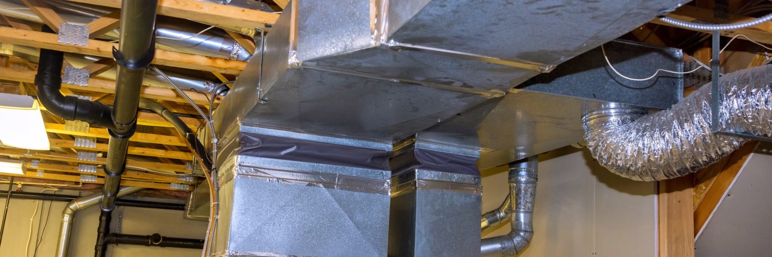 The basement of a home with metal ductwork and piping for an HVAC system attached to the ceiling joists.