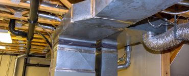 The basement of a home with metal ductwork and piping for an HVAC system attached to the ceiling joists.