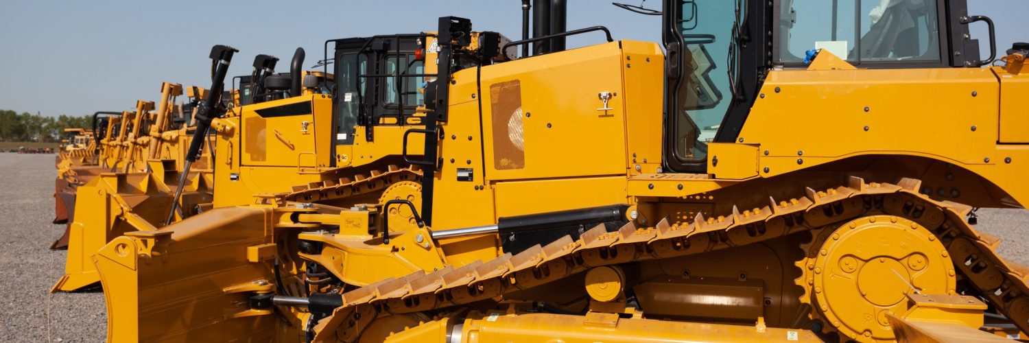 A row of yellow bulldozers parked on a construction site. The ground is flat with a layer of gravel.
