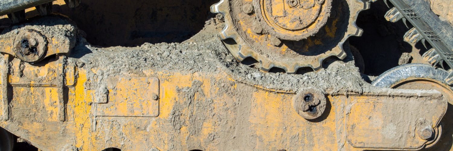 A close-up shows a bulldozer’s undercarriage with dried mud on the tracks and gears, lit by natural light.