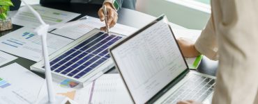 Two people standing around a table and examining documents and models with information about renewable energy options they could use.