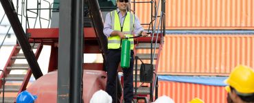 A man standing on a crane car while holding a fire extinguisher. There are employees watching him from the ground.