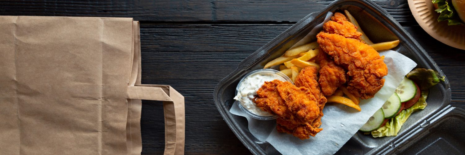 An assortment of fast food offerings in to-go or delivery packaging sitting on a black wooden table.