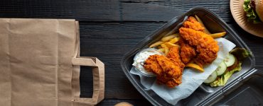 An assortment of fast food offerings in to-go or delivery packaging sitting on a black wooden table.