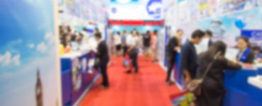 A blurred view of a crowd standing on a red carpet, surrounded by blue pop-up booths for a trade show.