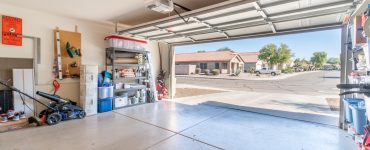 A garage with the exterior door open. There are various tools and boxes stacked against the garage wall.