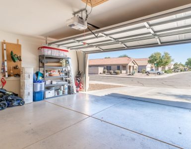 A garage with the exterior door open. There are various tools and boxes stacked against the garage wall.