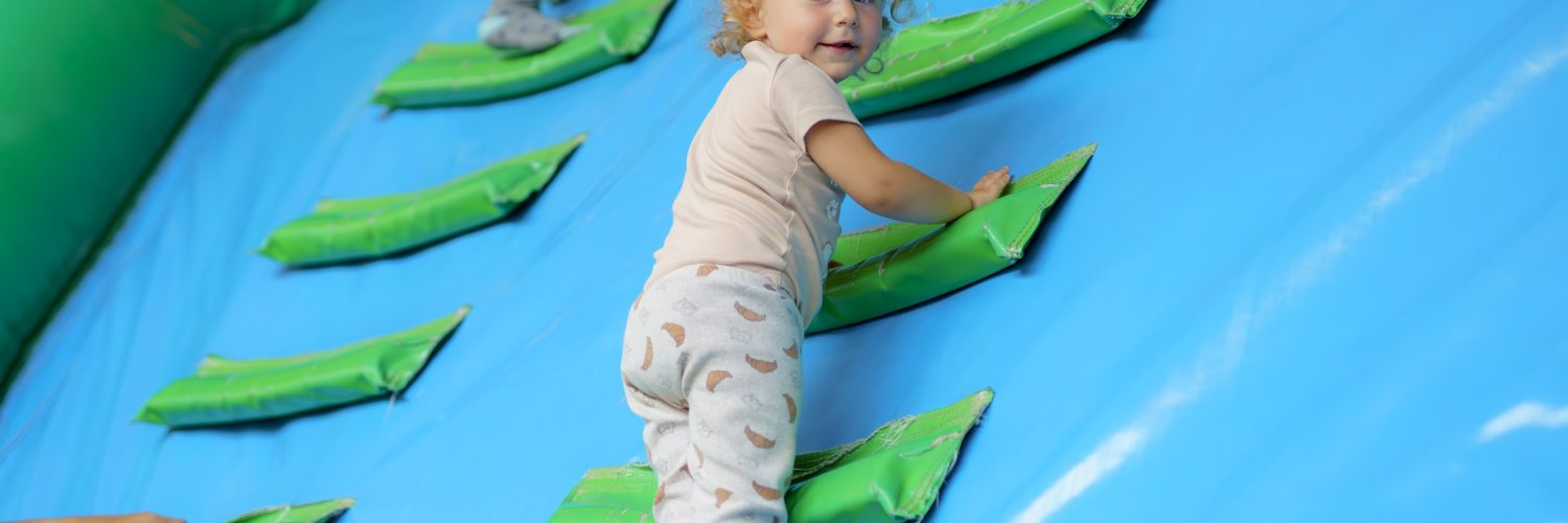 A toddler climbs soft green steps attached to a blue inflatable play structure.