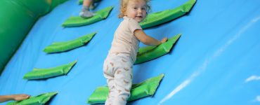 A toddler climbs soft green steps attached to a blue inflatable play structure.